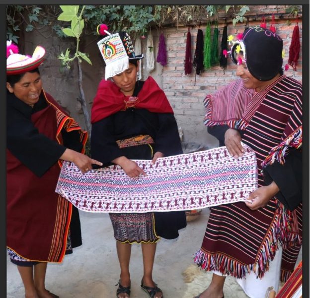 Three people in traditional dress examine the zigzag pattern at the heart of a Yampara weaving